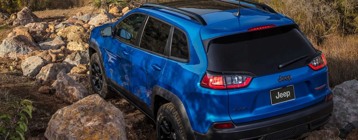 A blue 2022 Jeep Cherokee Trailhawk is shown from the rear while driving over rocks.