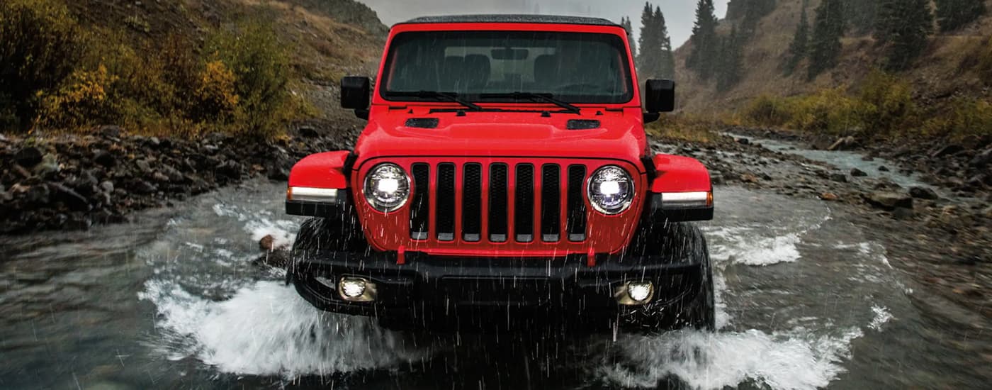 A red 2022 Jeep Wrangler Rubicon is shown off-roading through a river after leaving a Jeep dealer near Vineland.