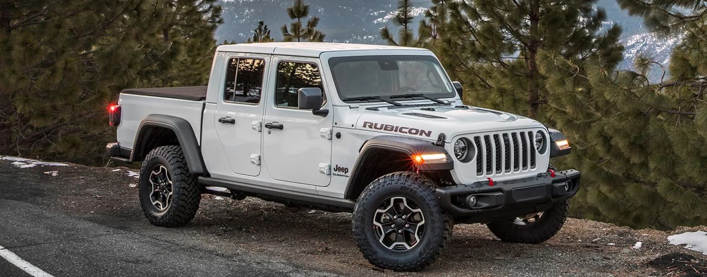 A white 2023 Jeep Gladiator Rubicon is shown parked on the side of a road next to trees.