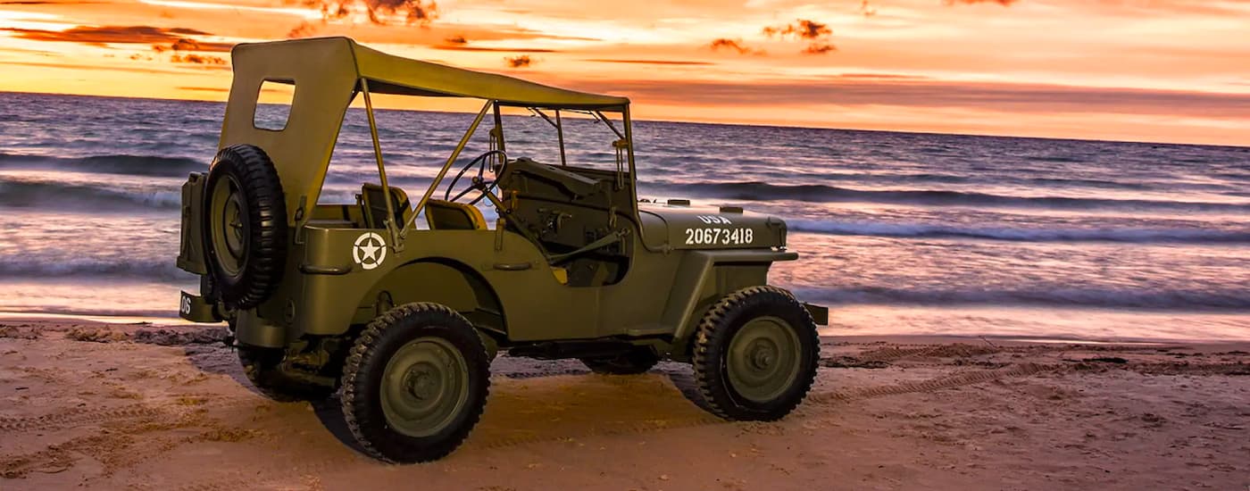 An olive green 1942 Jeep Willys is shown on the beach.
