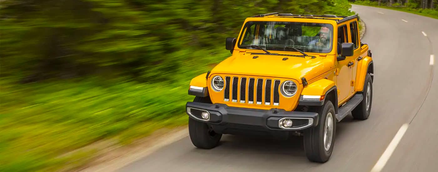 A yellow 2021 Jeep Wrangler Unlimited is shown driving on a wooded road.