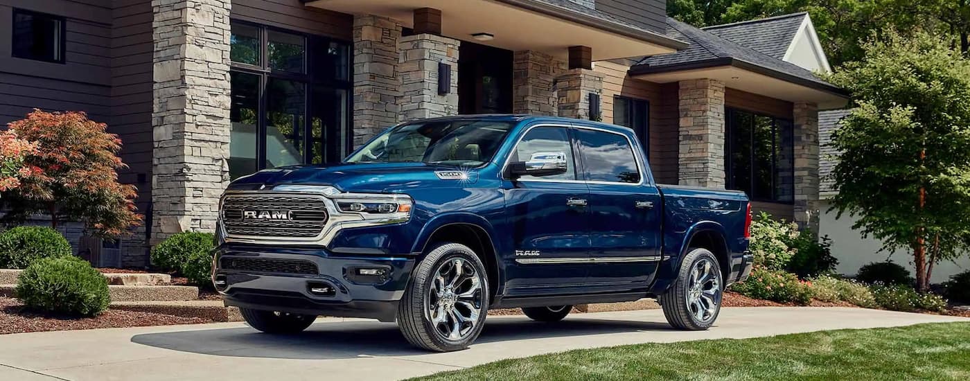 A blue 2023 Ram 1500 is shown parked in a driveway in front of a house with stone pillars.