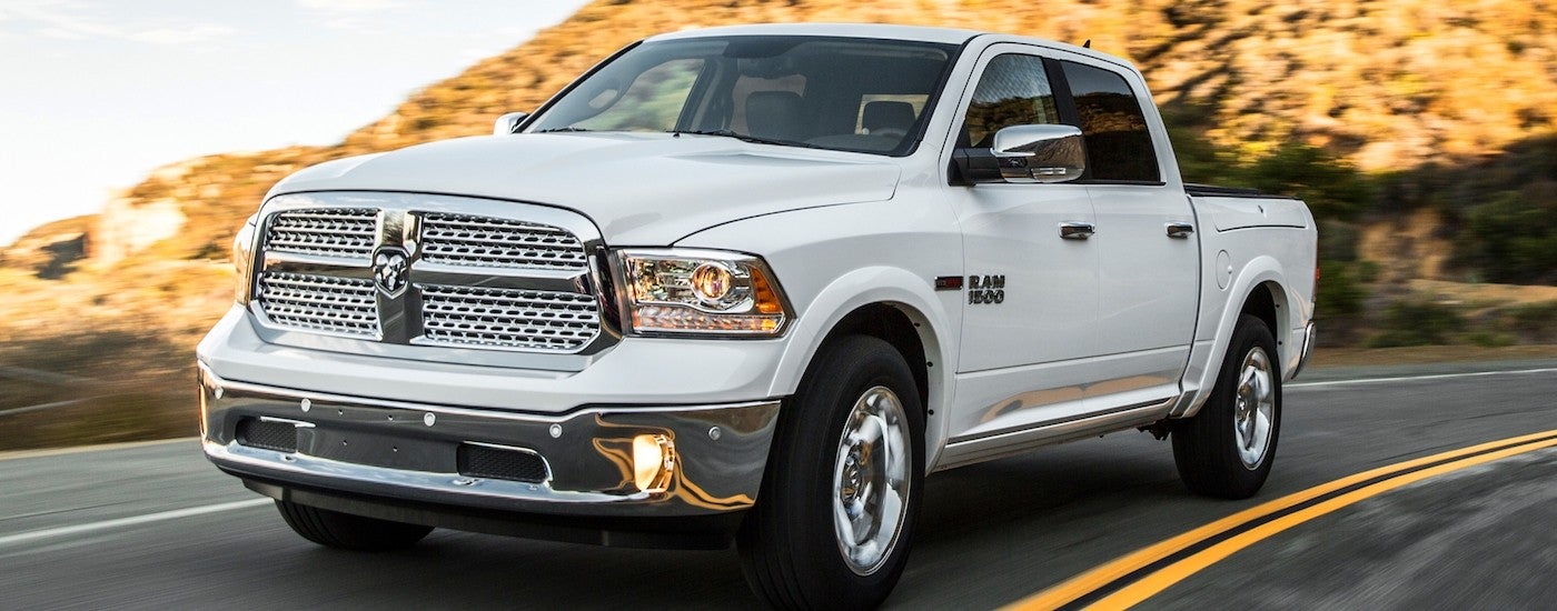 A white 2014 Ram 1500 is shown driving on a highway through a desert.