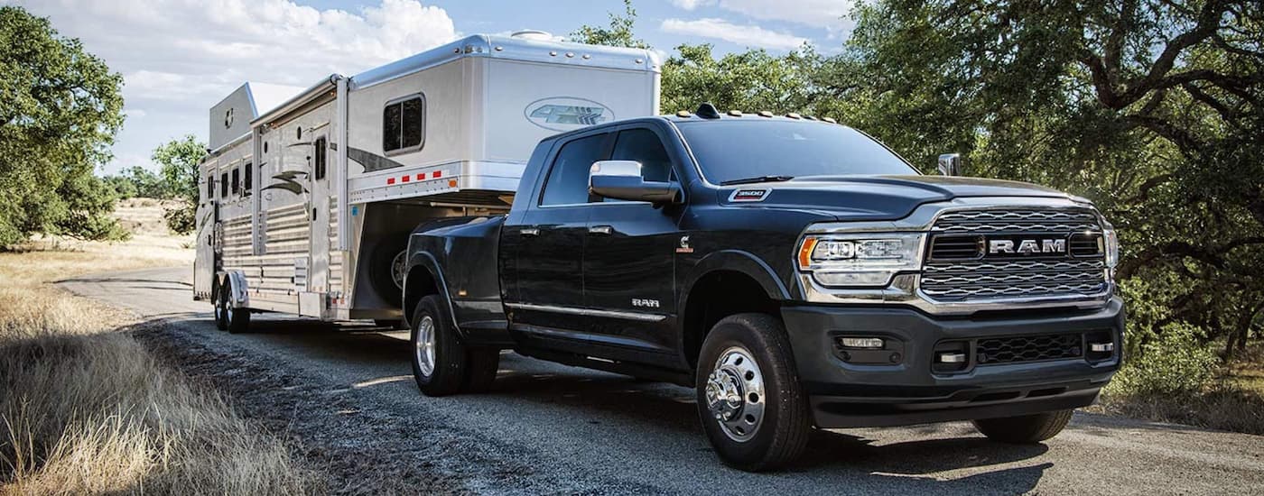 A black 2019 Ram 3500 is shown towing a white camper to a camping site.
