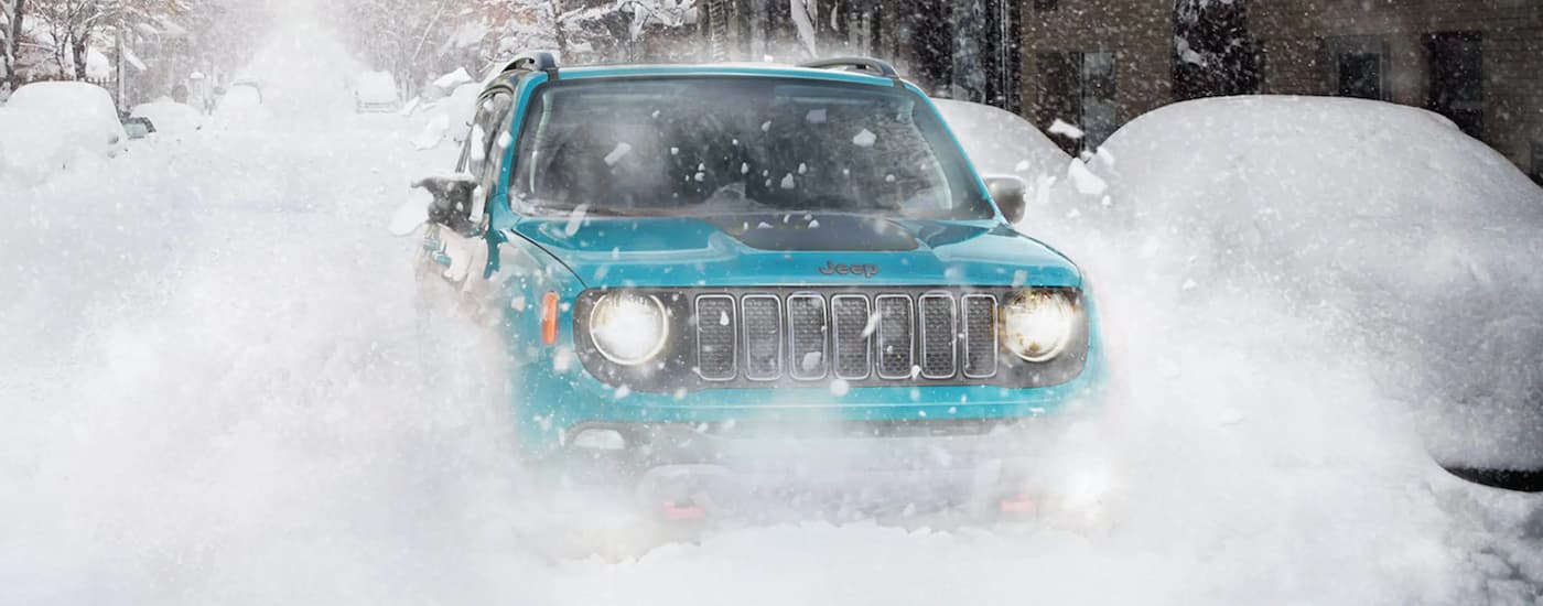A teal 2022 Jeep Renegade Trailhawk is shown driving through the snow.